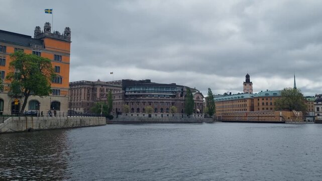 Panoramic view over the Norrstr&ouml;m river in Stockholm, Sweden, featuring the Ministry of Justice, the Swedish Parliament, and Vasabron bridge under a cloudy spring sky