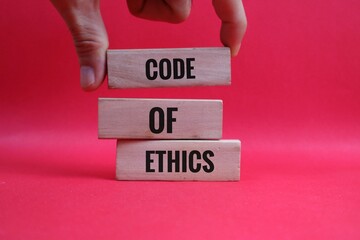 hand holding wooden block representing Code of Ethics writing on red background for Professional Concept
