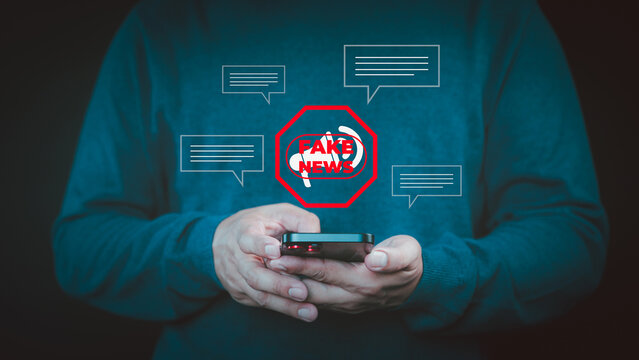 Fake News concept. Person holding a smartphone with a red "FAKE NEWS" warning icon surrounded by chat bubbles, symbolizing misinformation online, manipulate opinion on internet and social media. - Powered by Adobe