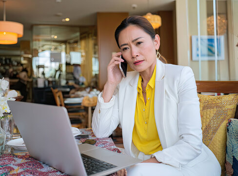 Asian businesswoman talking on phone with laptop in cafe, showing concern and focus