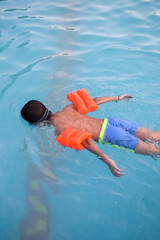 Happy Indian boy swimming in a pool, Kid wearing swimming costume along with air tube during hot summer vacations, Children boy in big swimming pool.