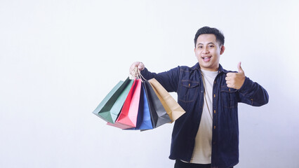 Portrait of smiling Asian man holding shopping bags and showing OK sign gesture with hand isolated on white background