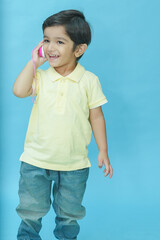 Indian child boy playing using toy mobile phone isolated against blue background. 2-3 year playful kid wear trendy blue jeans and t-shirt having fun. Childhood. Fashion. Copy space