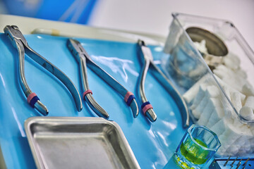 Dental tools arranged on a blue surgical tray, featuring extraction forceps, cotton rolls, and a...