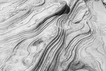 Monotone image of sculpted sandstone rock showing organic curves and striated patterns formed by...