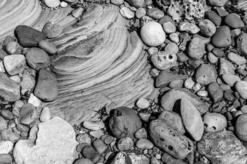 Textured arrangement of rounded pebbles and weathered stones surrounding a smooth, layered...