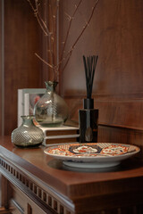 Classic home decor with a reed diffuser, glass vases, and an oriental ceramic plate on a dark wood...