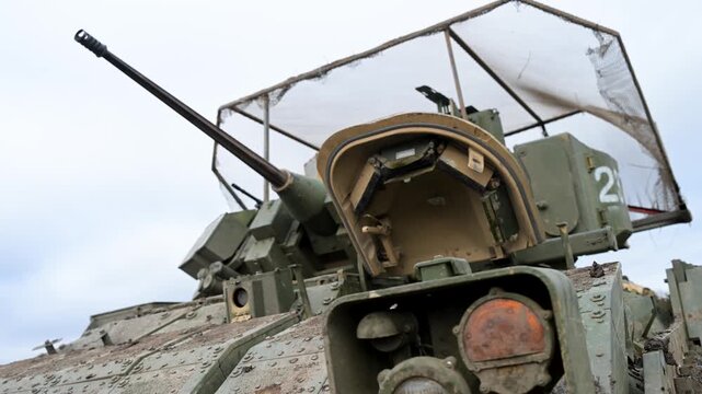 A low-angle close-up of the 25mm Bushmaster autocannon on a US-made M2 Bradley IFV during a training exercise in Ukraine. A 'cope cage' is visible above the turret.
