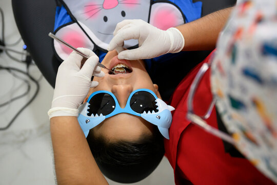 Pediatric dentist examining teeth of young boy wearing funny glasses - Powered by Adobe