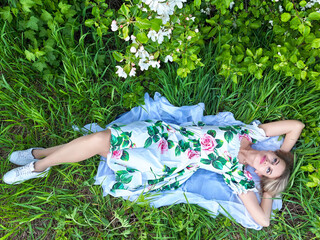 Blonde woman in floral dress posing in a lush green setting, enjoying a peaceful lifestyle moment outdoors