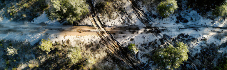 Aerial view of rugged muddy mountain trail with deep tracks under golden sunrise light, morning mist and fog creating dramatic topographic map effect in wilderness landscape.