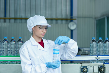 Technician inspecting bottled water on production line in beverage factory, wearing hygiene suit and gloves for quality assurance. Clean production concept