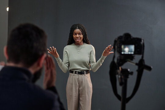 Young adult Black woman standing in front of camera performing expressive audition gestures while casting director observing, auditioning for acting role in professional studio setting