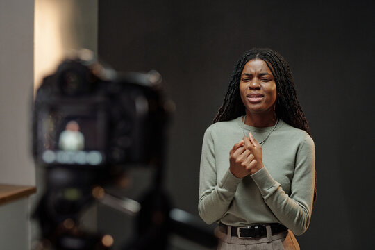 Black young adult woman performing emotional monologue during acting audition, standing in front of camera with expressive facial expression and hands clasped together
