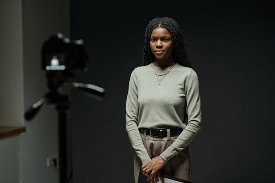 Portrait of young adult Black woman standing in front of camera holding script during acting audition, maintaining confident posture and direct gaze, participating in casting process