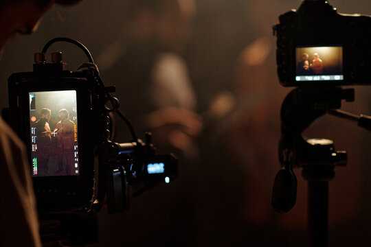 Two men standing together reading script during acting audition, being filmed by professional video camera, camera monitor displaying scene in foreground