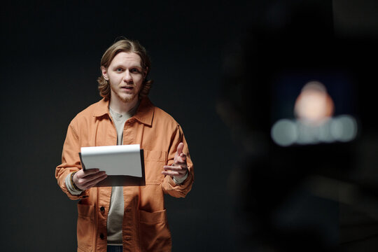 Caucasian young adult man standing on stage holding script performing monologue during acting audition facing camera with expressive gesture and focused facial expression