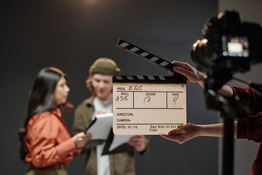 Young adult Caucasian man and young adult Hispanic woman standing together reading scripts during acting audition while camera and clapperboard visible in foreground capturing scene