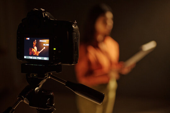 Young adult Hispanic woman standing in front of camera holding script, performing monologue during acting audition, digital camera on tripod recording audition process in studio