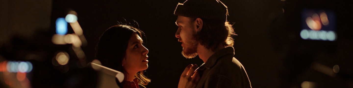 Young adult Caucasian man and young adult Hispanic woman performing dramatic scene together during acting audition on stage with professional cameras recording their interaction