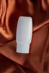 Cosmetic product in tube, bottle, lotion or serum on shiny cloth background