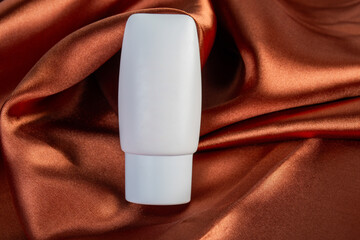 Cosmetic product in tube, bottle, lotion or serum on shiny cloth background