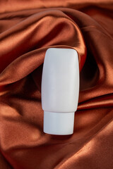 Cosmetic product in tube, bottle, lotion or serum on shiny cloth background
