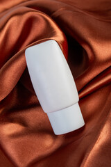 Cosmetic product in tube, bottle, lotion or serum on shiny cloth background