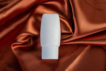 Cosmetic product in tube, bottle, lotion or serum on shiny cloth background