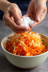 Woman's hands mixing shredded cabbage and carrot with salt for homemade sauerkraut. 
