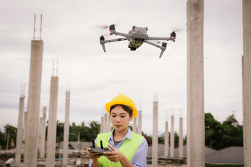 A female construction worker in a safety vest and hard hat operates a drone on-site, using smart technology for surveying, inspection, and monitoring in modern engineering projects.