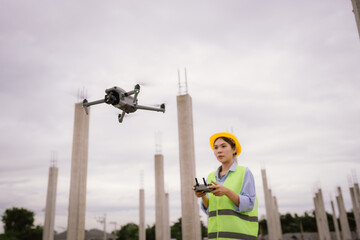 A female construction worker in a safety vest and hard hat operates a drone on-site, using smart technology for surveying, inspection, and monitoring in modern engineering projects.