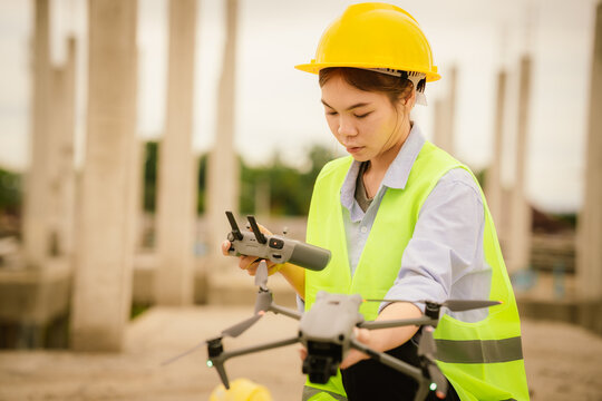 A female engineer in a hard hat and safety vest operates a drone at a construction site, using smart technology for inspection, surveying, and modern infrastructure planning.