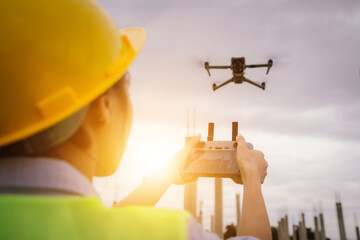 A female construction worker in a safety vest and hard hat operates a drone on-site, using smart technology for surveying, inspection, and monitoring in modern engineering projects.