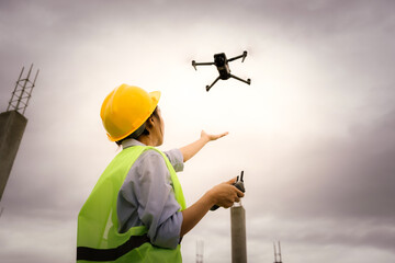 A female construction worker in a safety vest and hard hat operates a drone on-site, using smart technology for surveying, inspection, and monitoring in modern engineering projects.