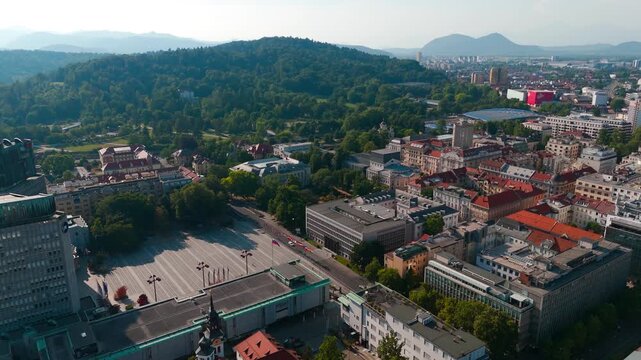 Aerial Establishing Shot of Slovenian Parliament Building in Ljubljana city. Green hills in distance. Sunny day with green trees in summer. Historic old town buildings.