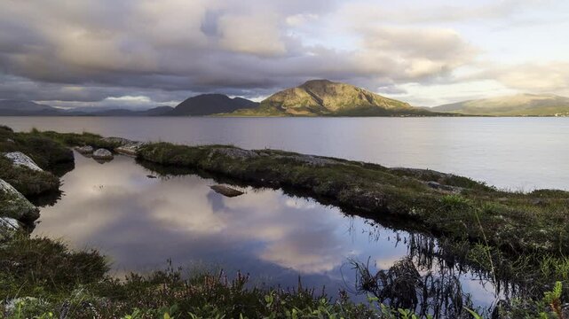 Beautiful landscape time-lapse near Torghatten in Bronnoysund in Norway. Clouds moving right to left and are reflected in the water. A small pond next to the ocean.