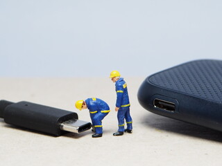 Mini toy of action figure at table with blurred background. Miniature photography concept design. Minifigure of engineer character fixing the USB port device.