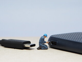 Mini toy of action figure at table with blurred background. Miniature photography concept design. Minifigure of engineer character fixing the USB port device.