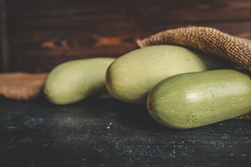 Fresh bottle gourds on dark table surface with rustic sackcloth and wooden background. Organic harvest displayed in natural light, perfect for healthy cooking or farm-themed visuals