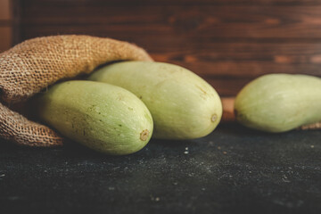 Fresh bottle gourds on dark table surface with rustic sackcloth and wooden background. Organic harvest displayed in natural light, perfect for healthy cooking or farm-themed visuals