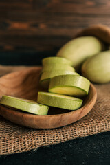 Round slices of bottle gourd in a wooden bowl placed on burlap fabric with whole gourds in the...