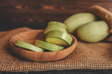 Round slices of bottle gourd in a wooden bowl placed on burlap fabric with whole gourds in the...