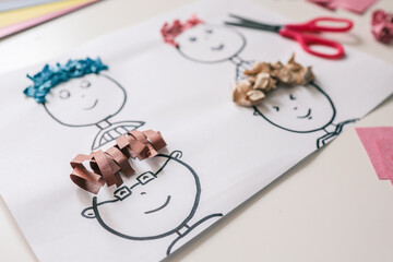 Children’s paper craft project with cartoon faces and colorful textured paper hair. Fun and...