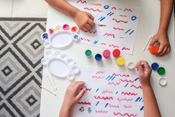 Children painting colorful lines and patterns on white paper using cotton swabs and jars of paint....