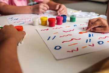 Children painting colorful lines and patterns on white paper using cotton swabs and jars of paint....