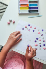Child making a colorful balloon artwork from clay dots on paper. Purple, pink, and white modeling...