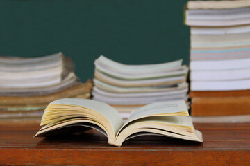 An open book ready to be read is placed on a wooden table with a blurry stack of books in the background.