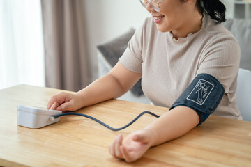 An Asian woman uses a portable blood pressure monitor in her living room. Health awareness concept.