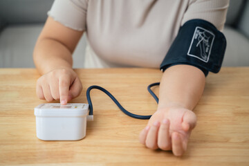 An Asian woman uses a portable blood pressure monitor in her living room. Health awareness concept.